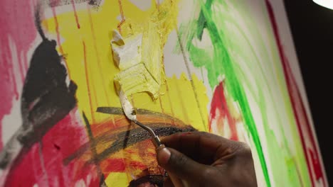 close up of hand of male artist painting with palette knife on canvas at art studio