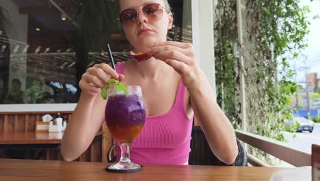 mujer disfrutando de una bebida púrpura y fruta en un café