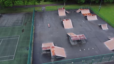 aerial view flying rising orbit above fenced skate park ramp and tennis court in empty closed playground