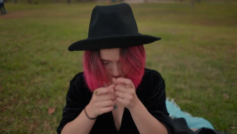 woman with pink hair wearing a black hat in a park