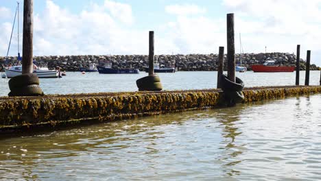 Weathered-wooden-harbour-dock-walkway-on-sunny-North-Wales-calm-sea-tide-slow-left-dolly