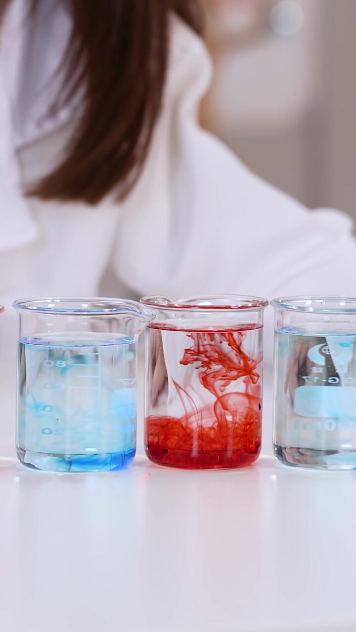 Primo piano di uno studente che aggiunge liquido colorato a becher durante un esperimento scientifico in classe STEM