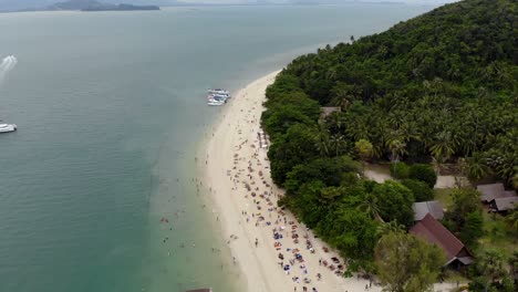 Vuelo-Aéreo-Sobre-La-Isla-Tailandesa-En-Un-Día-Nublado-Mientras-La-Gente-Nada-En-La-Playa,-Phuket