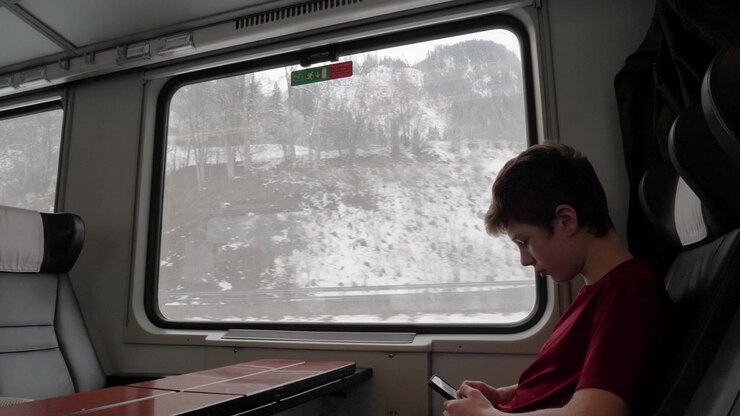 Young boy texting on his mobile phone and missing out the beautiful snow covered view from the glass window of moving train.