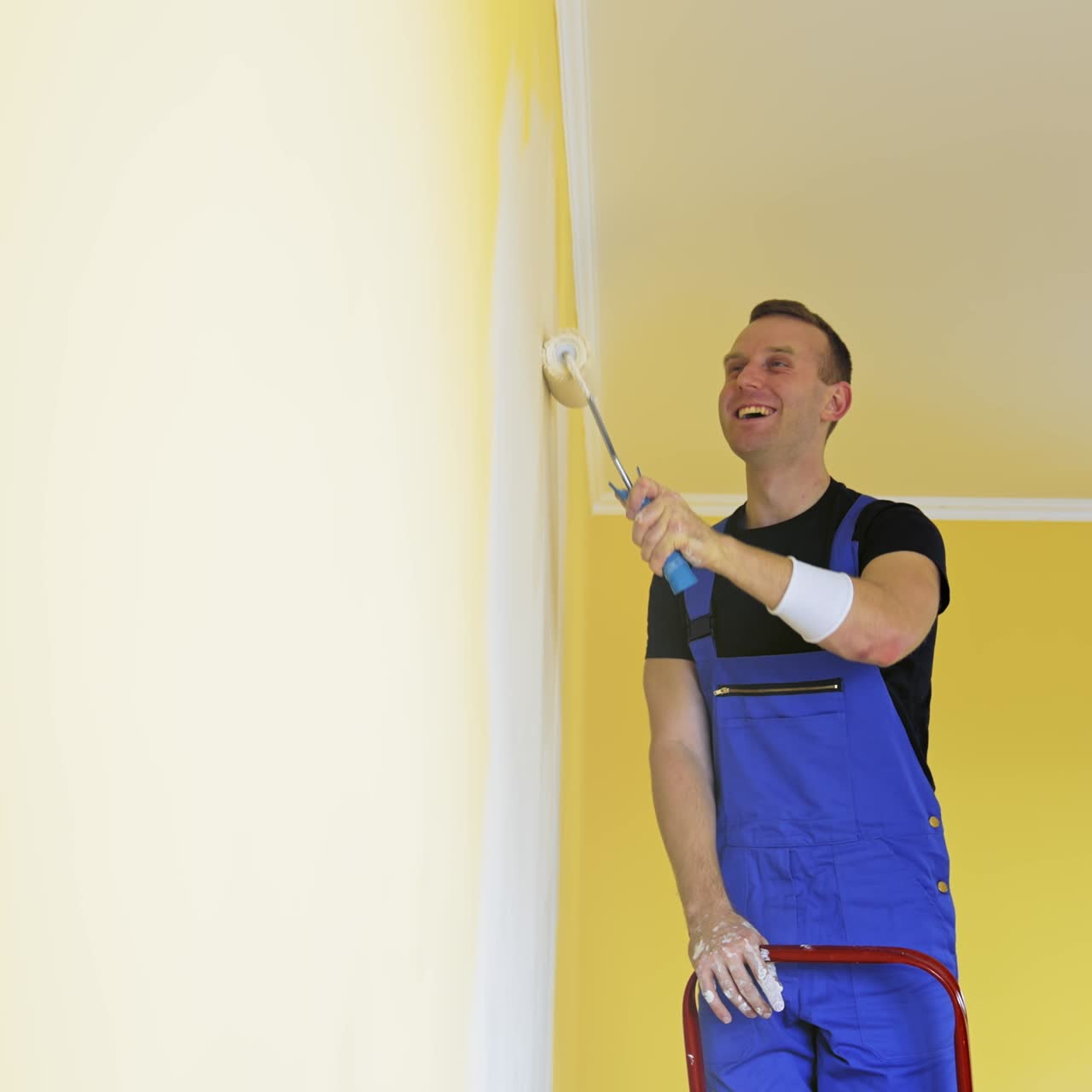 Attractive handsome repairman doing renovation the wall. Painter man at work painting an orange wall with a roller