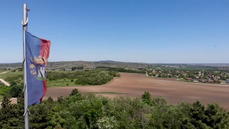 Aufsteigende-Und-Drehende-Drohnenaufnahme-Einer-Flagge-Mit-Burg-In-Zeitlupe