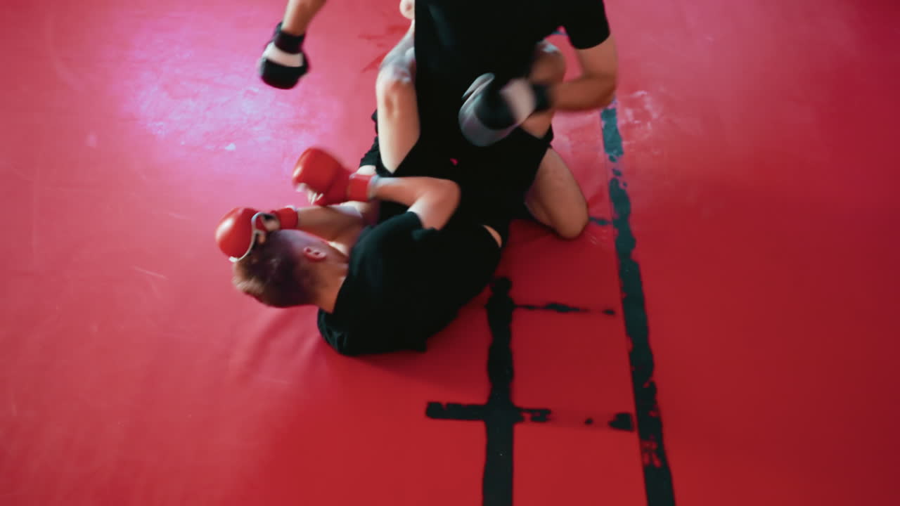 Combatants engaged in intense grappling on red mat during martial arts ground fight training,and punches showcasing endurance, control, skill, strength, and resilience in physical sparring practice