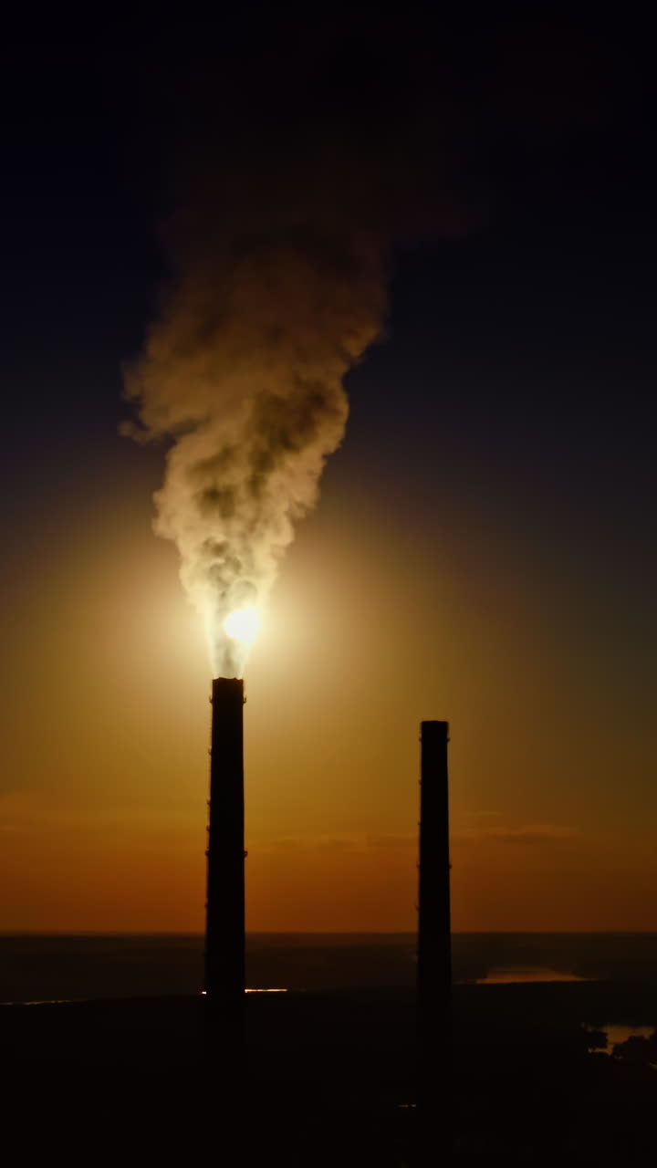 Dense smoke from pipes at sunset. Massive fumes released from industrial chimney into the environment. Nature in danger. Vertical video