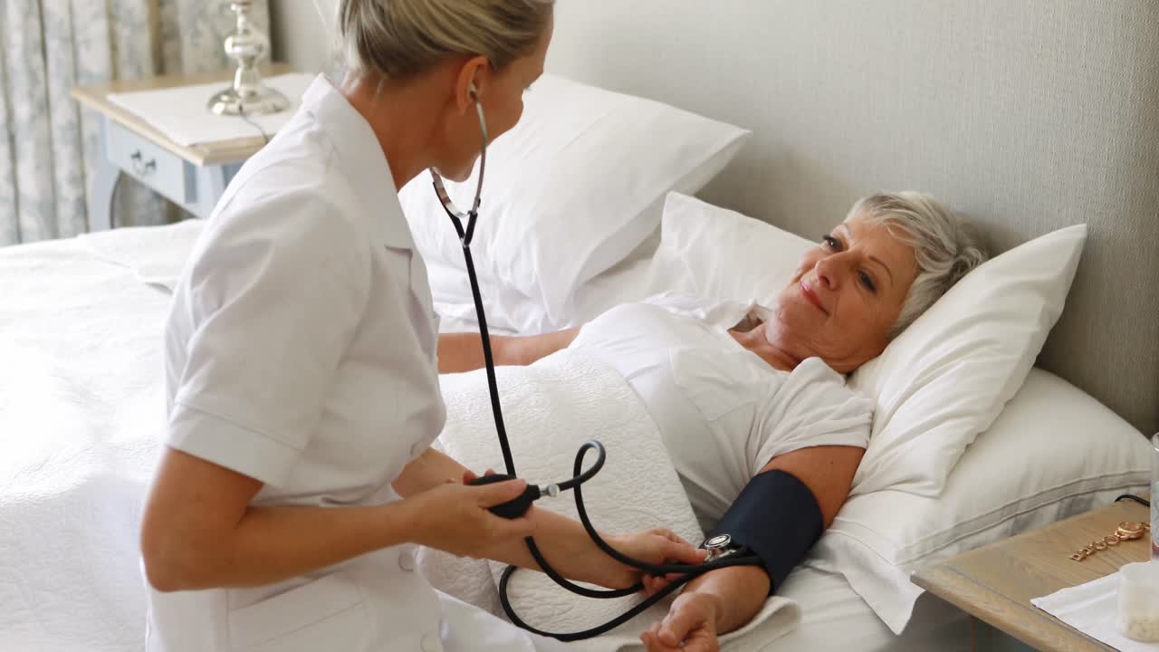 Female doctor checking the blood pressure of senior woman in the bedroom