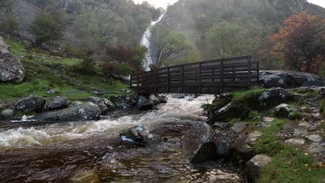 Waterfall-rocky-river-powerful-flowing-water-slow-motion-cascading-under-wooden-bridge-in-national-park