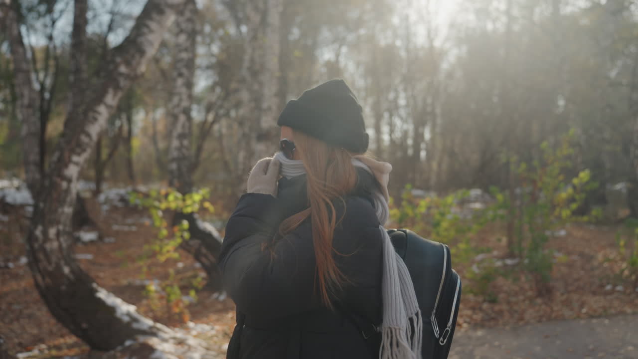 Vaaleaihoinen reppumatkailija kävelee metsäpolulla, naamioituneena ja vilkuillen olkapään yli syksyisen auringonvalon alla koivikkomaisemassa. Varovainen tahti ja jännittynyt asento vihjaavat piilevään uhkaan.
