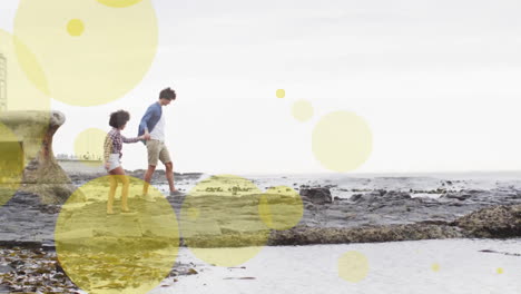 animation of light spots over biracial couple holding hands and walking on beach
