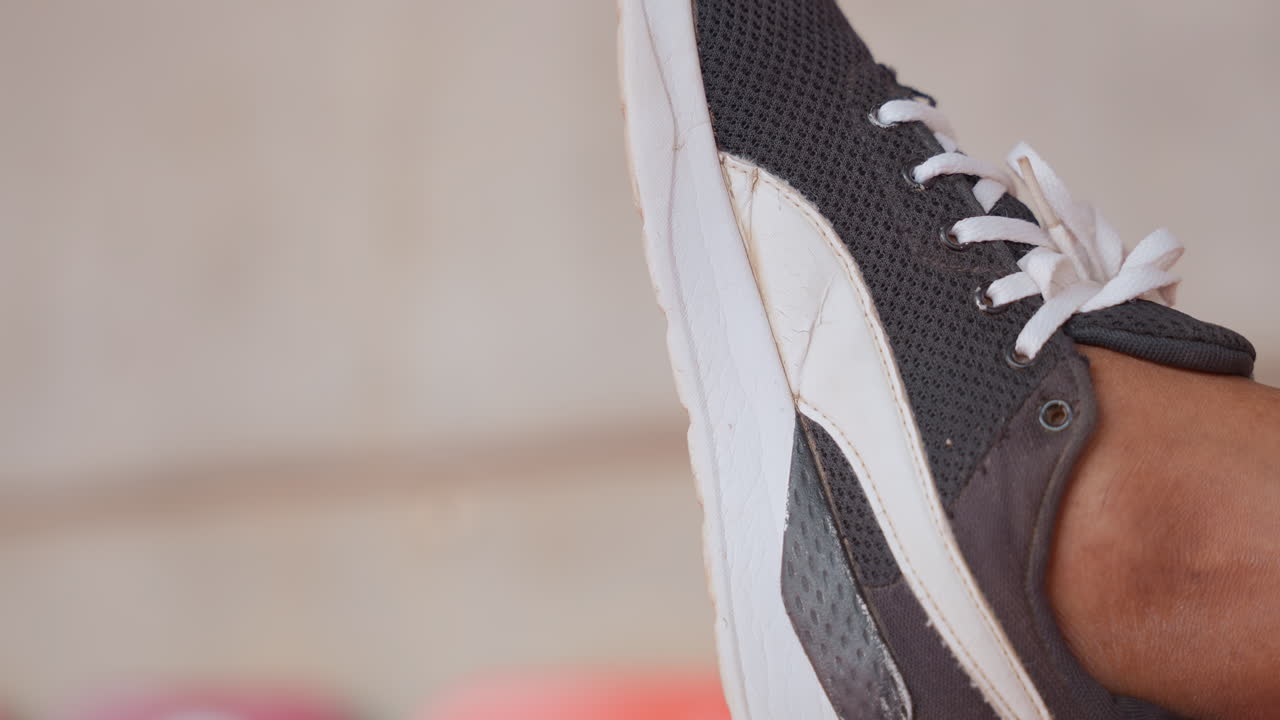 Primo piano di lacci di scarpe da ginnastica che mostrano tessuto testurizzato e suola usurata; un runner urbano si ferma su un marciapiede di cemento, passo rilassato, movimento sottile, luce naturale calda, sfondo bokeh morbido, stile casual.