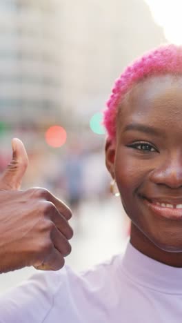 a young woman with pink hair smiles and gives a thumbs up in an urban setting