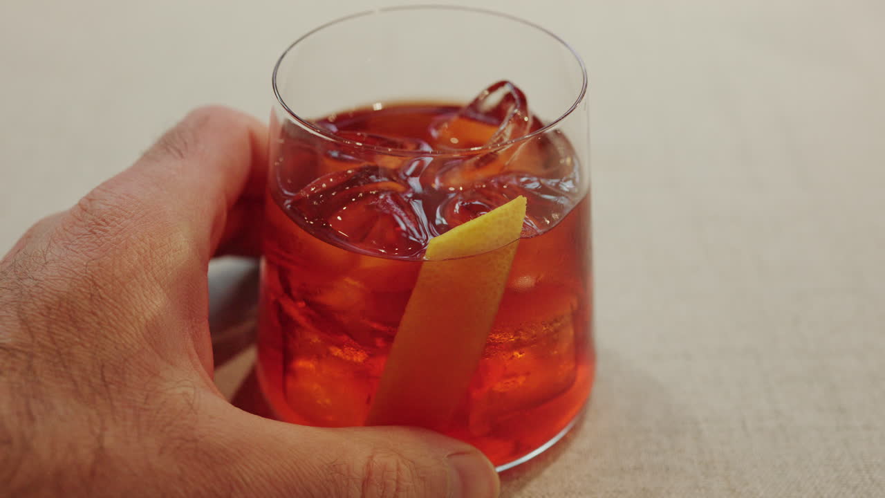 Primo piano di un uomo che tiene in mano un bicchiere da cocktail pieno di ghiaccio e una guarnizione di agrumi