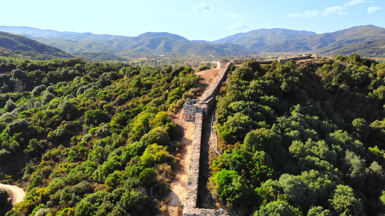 Vista aerea con drone della costa rocciosa del Mar Egeo, scavi di antiche mura su una collina, città sullo sfondo in Grecia