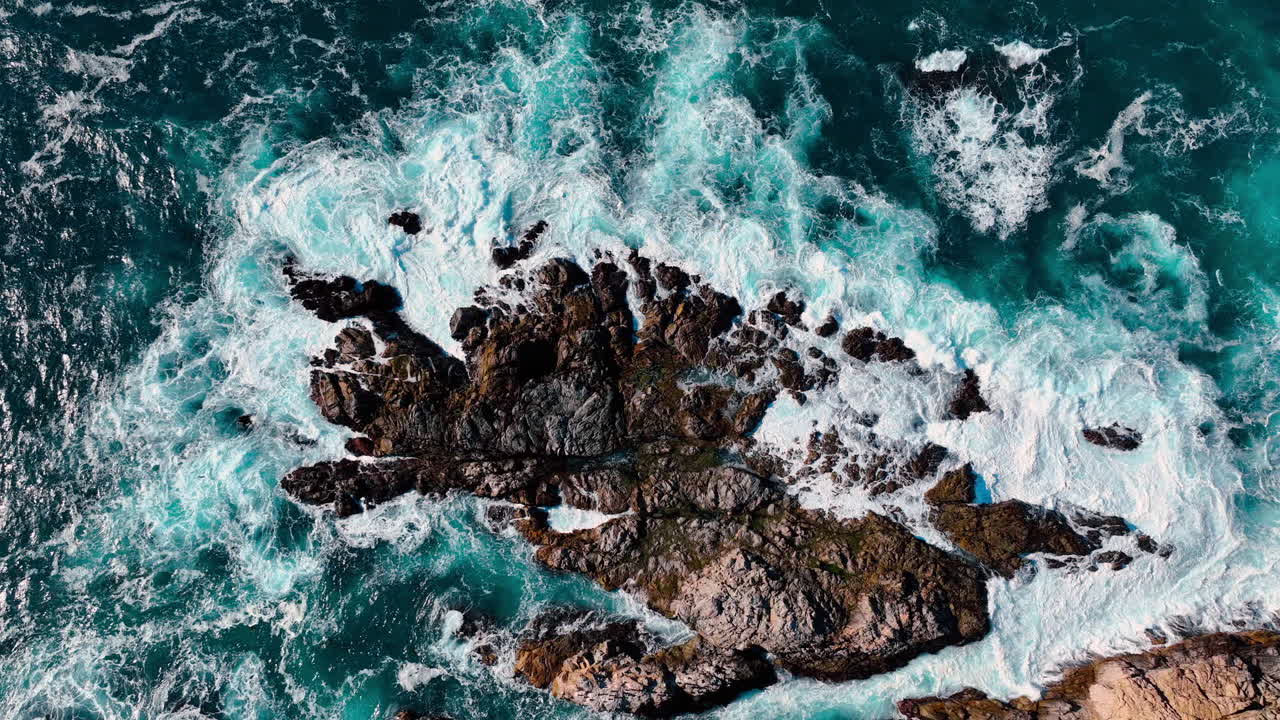 Vista aerea dall'alto della schiuma bianca delle onde sulle rocce. Veduta reale dall'alto dell'acqua turchese dell'Oceano Pacifico e delle onde che si infrangono sulla costa rocciosa a Big Sur, California.