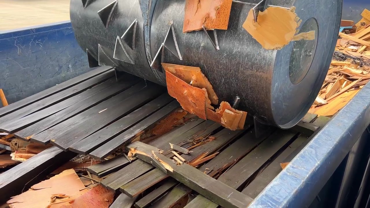 Rotierende Brechertrommel rollt über zerbrochene Holzabfälle im Wertstoffhof