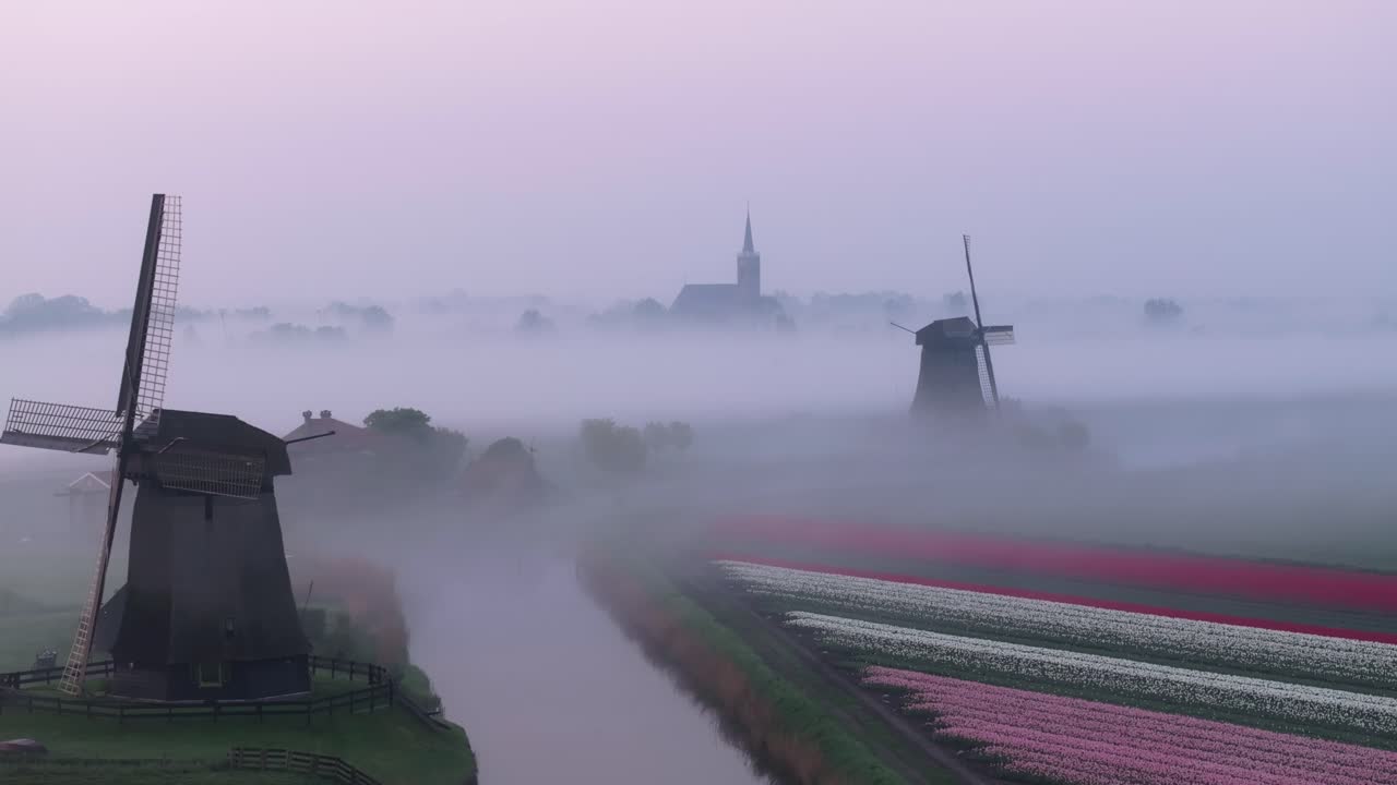 Veduta aerea della campagna olandese con nebbia, mulini a vento e una chiesa all'alba.