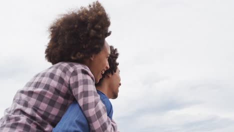 afrikaans-amerikaanse man geeft zijn vrouw een piggyback rit op de promenade bij het strand