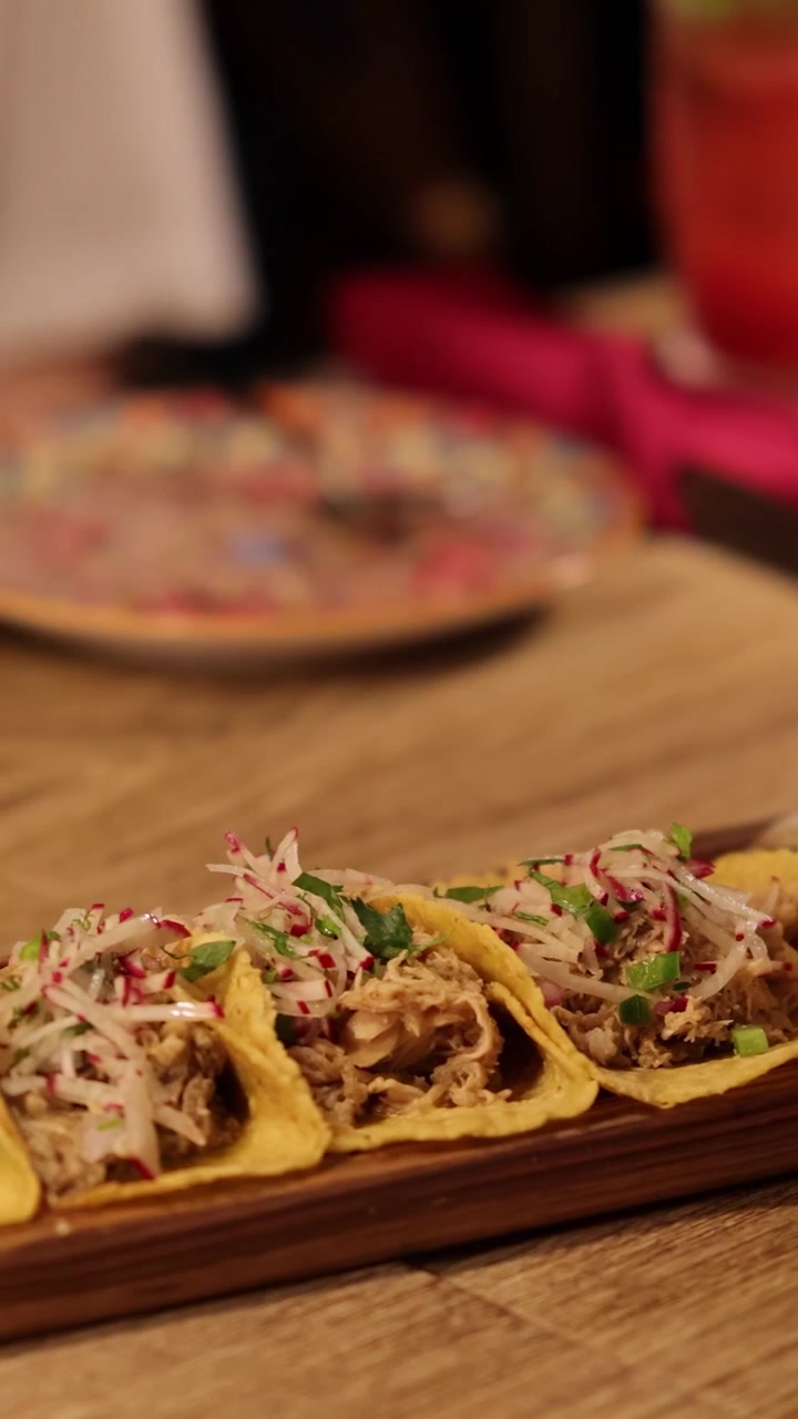 Primo piano di tacos su un vassoio di legno in un ambiente di ristorante in penombra, che evidenzia ingredienti vivaci e un'atmosfera calda.