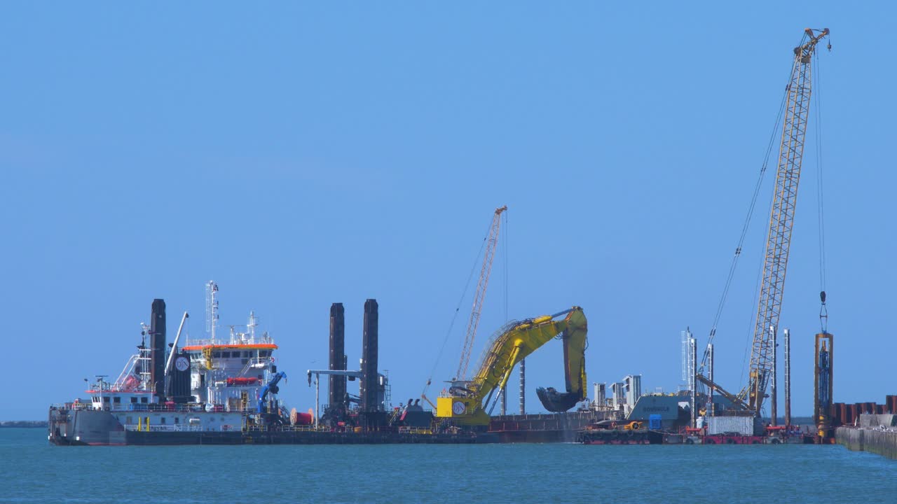 Hopper dredger ship working at Port of Liepaja, crane with bucket lifts up soil from the bay, medium shot from a distance