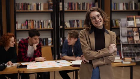 Retrato-De-Una-Atractiva-Estudiante-Europea-De-Pelo-Corto-Con-Gafas-Y-Chaqueta-Marrón-Parada-En-La-Biblioteca-De-La-Escuela-Secundaria-Sonriendo-Mirando-A-La-Cámara-Y-Sonriendo