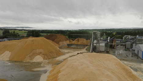 Aerial-over-sawdust-mountains-at-lumberyard,-Forestia-factory,-Braskereidfoss