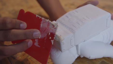 filling a hole in a plastic astronaut figure with filler and red spatula