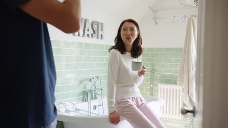 Mature-Asian-couple-wearing-pyjamas-sitting-in-bathroom-enjoying-morning-hot-drinks-together---shot-in-slow-motion