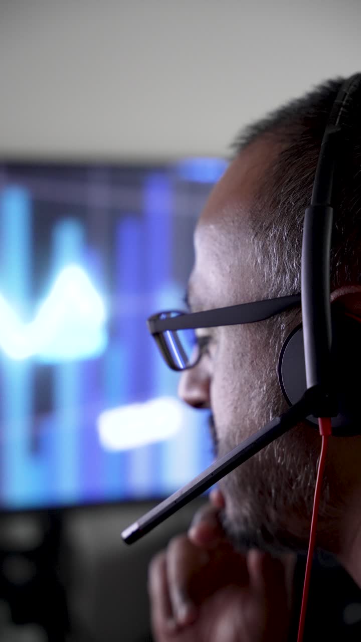 Close up of a focused indian programmer wearing a headset while working on his computer. vertical video