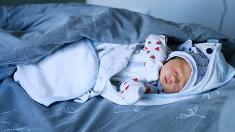 little cute caucasian baby in cap and romper sleeping in the blankets. few days old child after hospital.