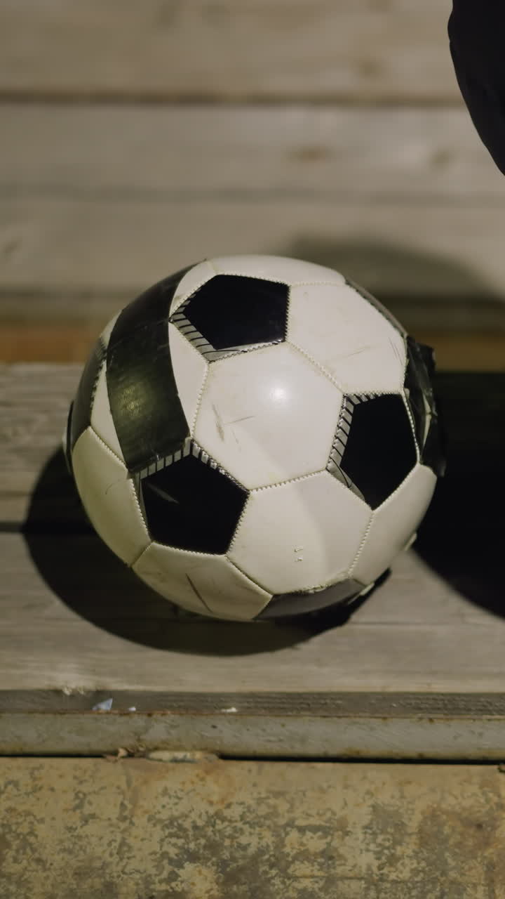 Close-up back view of a man in a black jacket seated quietly in a stadium, the man is sitting alone with his hands between his legs, and a soccer ball is placed close to him on the bench
