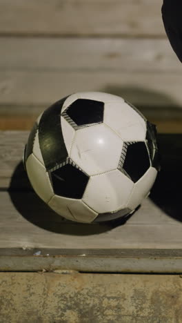 close-up vista de trás de um homem em uma jaqueta preta sentado quietamente em um estádio, o homem está sentado sozinho com as mãos entre as pernas, e uma bola de futebol é colocada perto dele no banco