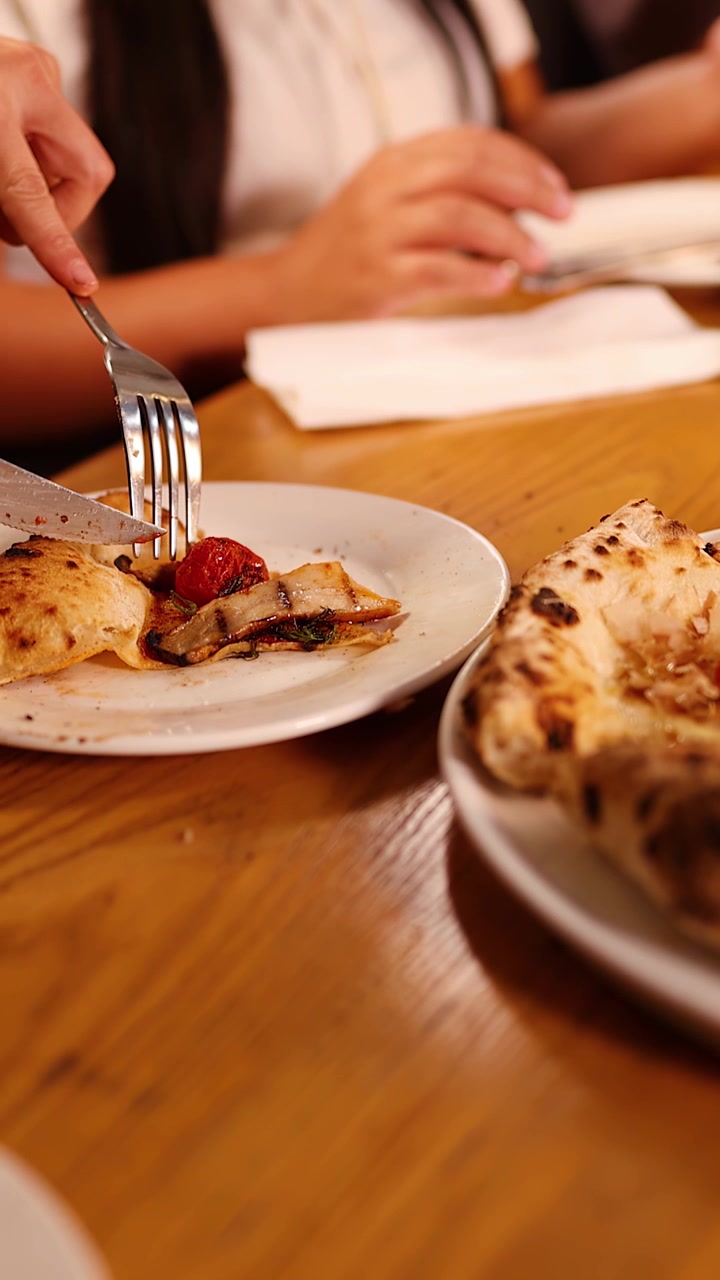 I commensali usano una forchetta e un coltello per tagliare pizza fresca su un tavolo di legno.