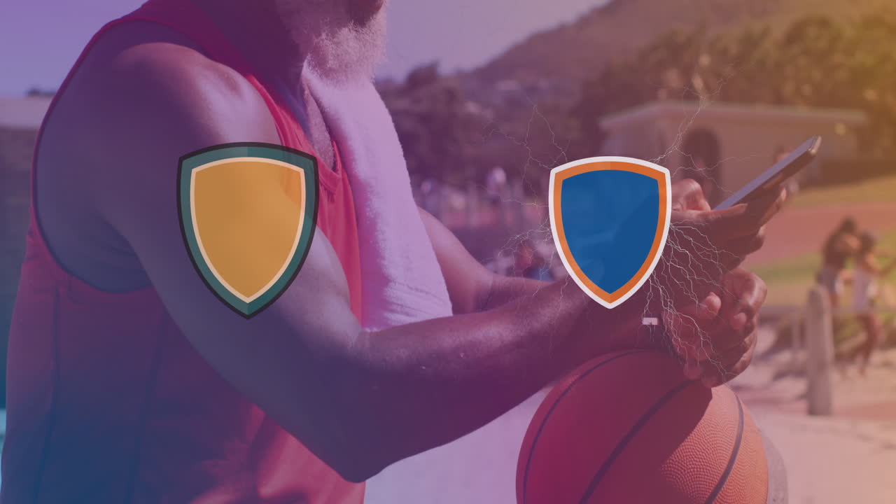 dos logotipos chocando contra un hombre mayor afroamericano con baloncesto usando un teléfono inteligente