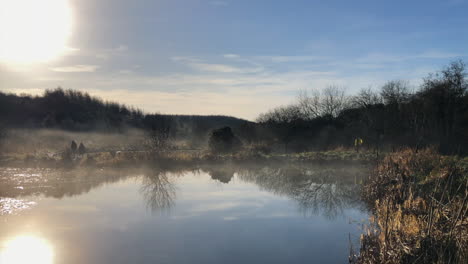 Two-people-enjoy-tranquil-walk-by-foggy-sunrise-pond,-cool-autumn-day