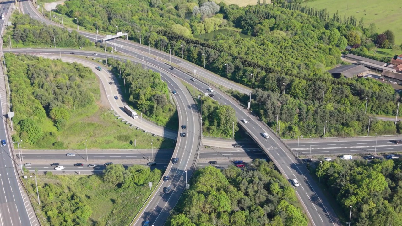 Vista aérea de un concurrido intercambiador de autopistas con vehículos circulando y congestión de tráfico. Árboles verdes y el paisaje rodean la compleja red de carreteras durante un día despejado.