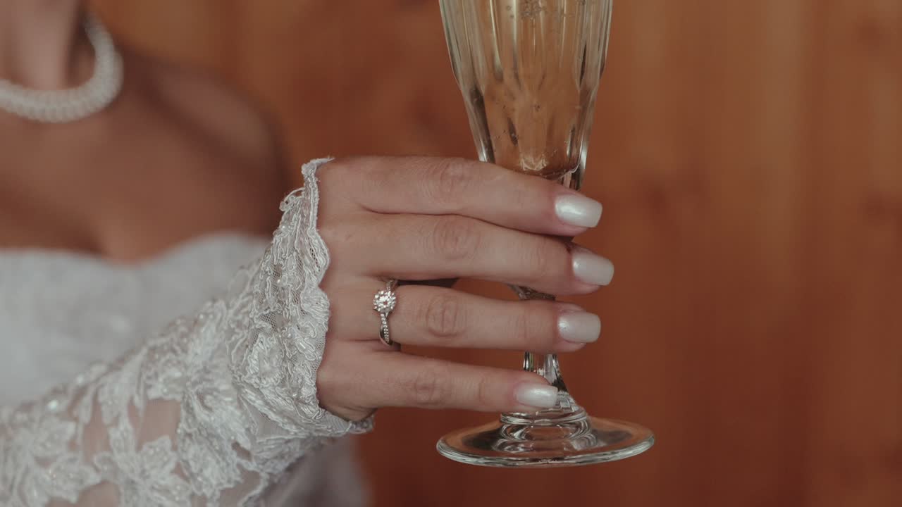 close up of bride’s hand with wedding ring holding champagne glass