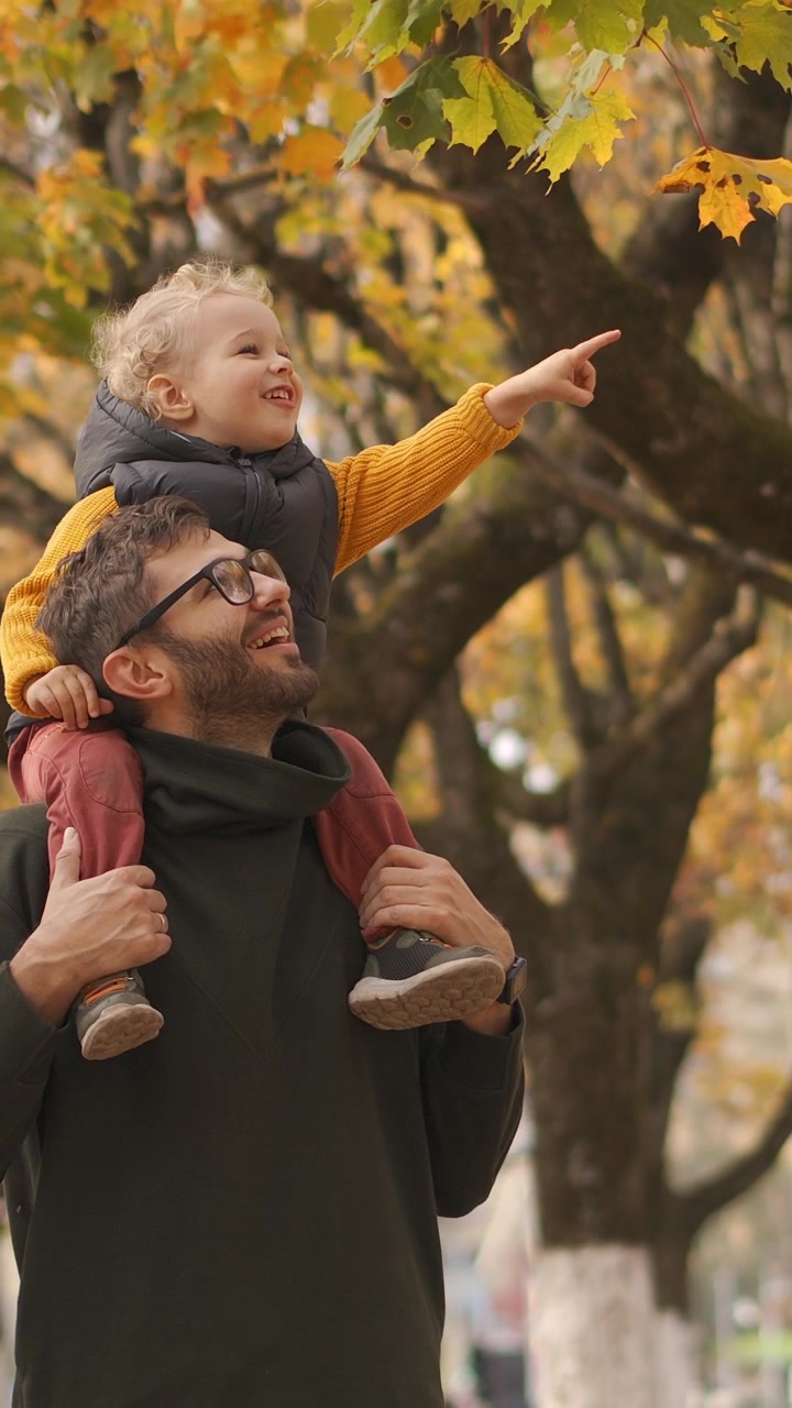 Padre che porta il figlio piccolo sulle spalle in un parco autunnale