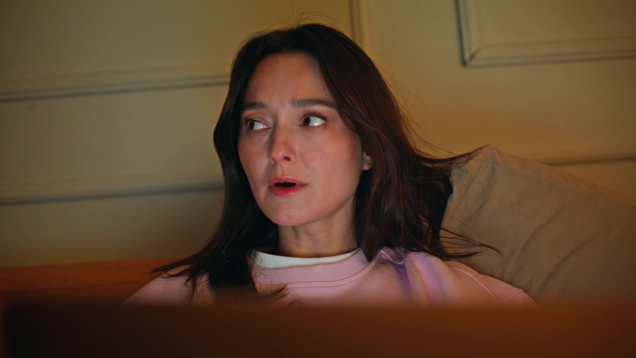 Nervous woman watching laptop in dark bedroom closeup. Dissatisfied brunette