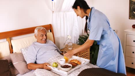 nurse serving breakfast to senior man in bedroom