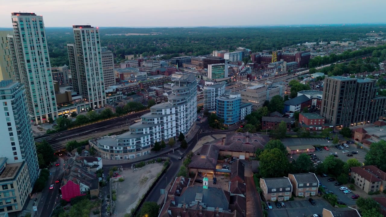Ciudad de Woking en Surrey, Inglaterra. Amplia vista aérea del centro de la ciudad al anochecer mostrando edificios de gran altura, desarrollo residencial, ferrocarril y regeneración urbana.