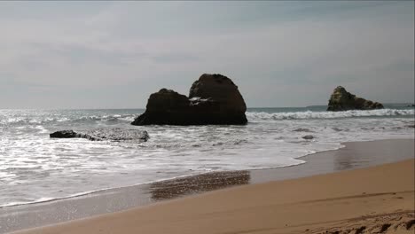 Praia-Do-Vale-Do-Olival,-Portugal-An-Einem-Bewölkten-Nachmittag-Mit-Bewölktem-Horizont-über-Wasser-Und-Wellen,-Die-In-Zeitlupe-Gegen-Riesige-Felsen-Schlagen
