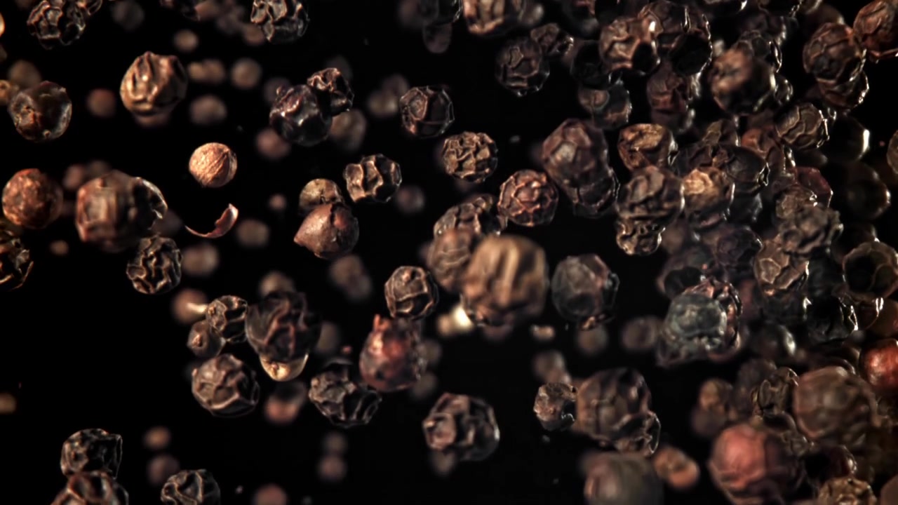 Svarte pepperkorn som faller i sakte film på svart bakgrunn