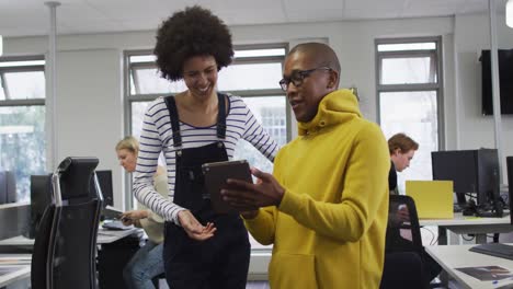 Diverse-smiling-male-and-female-business-colleagues-using-tablet-and-discussing-in-office