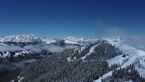 Hiking-trail-on-top-of-a-snowy-mountain,-clouds-in-the-valleys