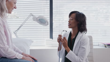 doctor listening to mature female patient breathing with stethoscope during medical exam in office