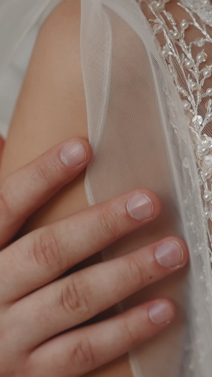 Man strokes arm of beloved bride wearing glam wedding dress with floral decor closeup slow motion. Young couple at bridal ceremony. Love relationship