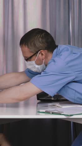 doctor and child sit at table, in protective masks, doctor tries to put thermometer to girl, but does not succeed, and he looks into camera, shaking head
